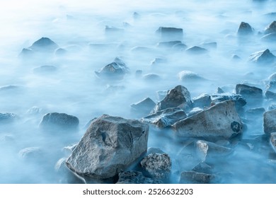 Misty waves caress the rocky shoreline at dawn in a tranquil coastal landscape - Powered by Shutterstock