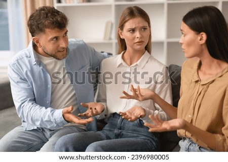 Misunderstanding In Friendship. Three Angry Friends Having Quarrel Arguing Sitting On Sofa At Home. Millennial Romantic Couple and Female Friend Engage in Heated Argument Having Conflict