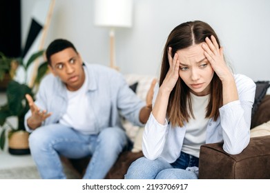 Misunderstanding In Relationships, Jealousy, Quarrel. Mixed Race Couple Sitting On A Sofa In The Living Room, An Angry Man Yells At A Woman, Feels Angry, Frustrated Sad Girl Turned Away From Him