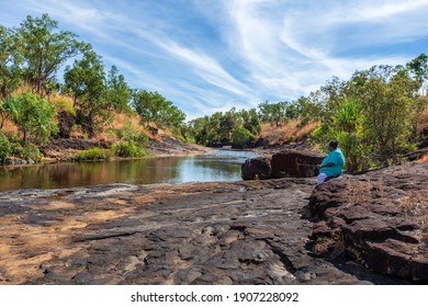 Mitchell Plateau, WA, Australia - May31, 2015: An Indigenous Australian Woman From The Local Kandiwal Community Sits Beside A Prisitne Outback River.