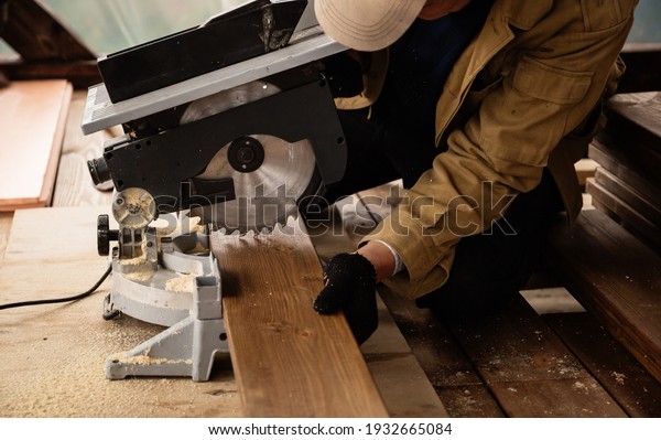 Miter saw with a large metal blade in the hands of\
a carpenter. Working tool for sawing wooden planks. A close-up of\
the sawing process. Labor protection and safety rules for the use\
of power tools.