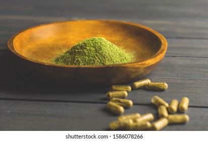 Mitragynina speciosa or Kratom powder in wooden bowl and Kratom capsules on table