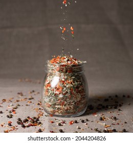 Mix of aromatic oriental spices and herbs being sprinkled in glass jar placed on table 