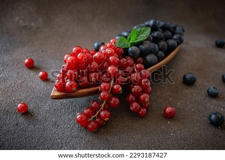 Mix of berries - blueberries and red current on wooden dish on dark brown background 