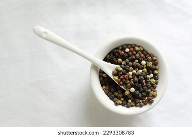 A mix of black, white, red and fragrant peppercorns in a white bowl on a light background. dried spice peppercorn concept. Vertical orientation. Selective focus. Copy space. Top view.