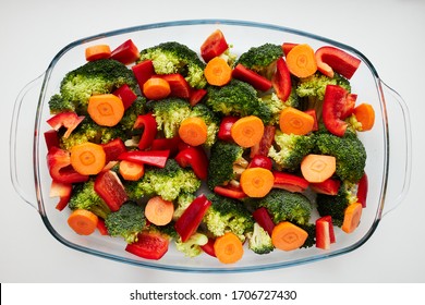 A Mix Of Broccoli, Bell Pepper (paprika) And Round Slices Of Carrot In The Glass Baking Dish On The White Table. 