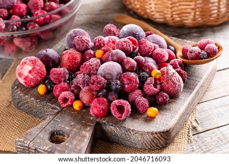 Mix of different frozen berries on a cutting board on wooden table. Frozen Food. Food storage