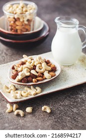 Mix of different nuts in a white bowl on a brown background with a carafe of milk