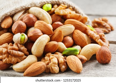 Mix of different nuts in a wooden cup against the background of fabric from burlap. Nuts as structure and background, macro. Top view.
