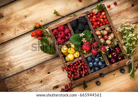 Mix of fresh berries with leaves in vintage wooden box on rustic wooden background. Top view. Raw healthy food. Assorted berries.