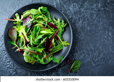 Mix fresh leaves of arugula, lettuce, spinach, beets for salad on a dark stone background. Selective focus.