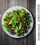 Mix of fresh organic juicy salad greens and red and yellow cherry tomatoes in grey plate on rustic wooden table. Food photography