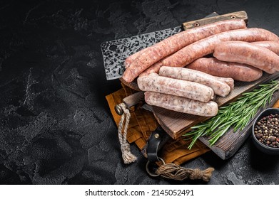 Mix fresh raw sausages. Beef, pork, lamb and chicken mince meat sausages on a butcher cutting board with spices. Black background. Top view. Copy space.