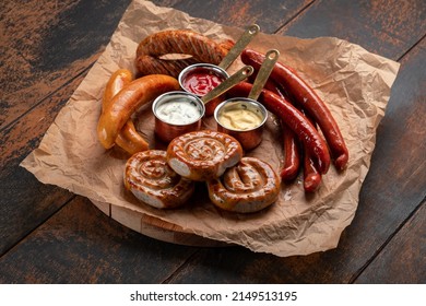 A mix of grilled sausages - Bavarian, round, Cumberland, bratwurst with ketchup and sauce on a wooden table. Traditional Bavarian Beer Snack