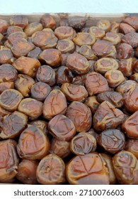 A mix of medium-sized, roundish dates are piled together in a box or tray, ready for consumption