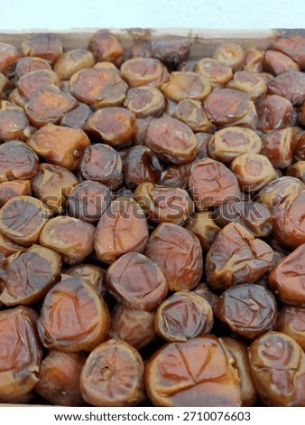 A mix of medium-sized, roundish dates are piled together in a box or tray, ready for consumption