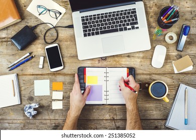 Mix Of Office Supplies And Gadgets On A Wooden Desk Background. View From Above.