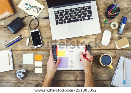 Mix of office supplies and gadgets on a wooden desk background. View from above.