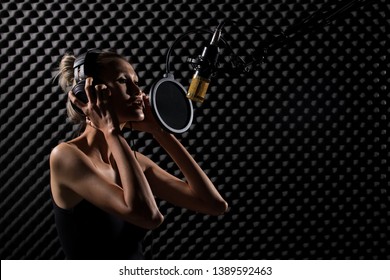 Mix Race Skinny Woman Blonde Short Hair Earmuff Headphone Sing A Song Loudly With Power Sound Over Hanging Microphone Condenser. Egg Crate Studio Low Lighting Shadow Sound Proof Absorbing Wall Room