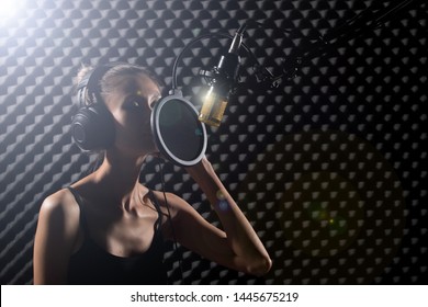 Mix Race Skinny Woman Blonde Short Hair Earmuff Headphone Sing A Song Loudly With Power Sound Over Hanging Microphone Condenser. Egg Crate Studio Low Lighting Shadow Sound Proof Absorbing Wall Room