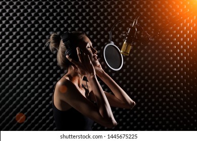 Mix Race Skinny Woman Blonde Short Hair Earmuff Headphone Sing A Song Loudly With Power Sound Over Hanging Microphone Condenser. Egg Crate Studio Low Lighting Shadow Sound Proof Absorbing Wall Room