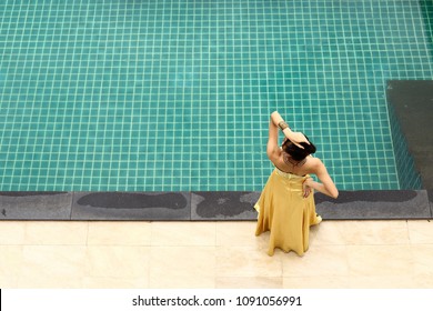 Mix Race Tanned Skin Woman In Yellow Gold Fashion Evening Gown Dress On The Edge Of Swimming Pool, Top View From Above, Happy Feeling Of Perfect Holiday Vacation Summer, Copy Space Text Logo