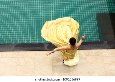 Mix Race Tanned Skin Woman In Yellow Gold Fashion Evening Gown Dress On The Edge Of Swimming Pool, Top View From Above, Happy Feeling Of Perfect Holiday Vacation Summer, Copy Space Text Logo