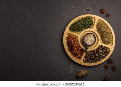 Mix spices on round wooden plate - coriander seeds, ground red pepper, salt, black pepper, rosemary, turmeric, curry. Top view, close up, gray stone background. - Powered by Shutterstock