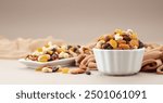 The mix of various nuts and raisins in a white bowl on a beige background.