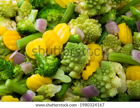 mix of various vegetables like broccoli, romanesco broccoli, yellow carrot slices, green beans and red onion pieces