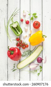 Mix Of Vegetables On White Planked Wood Background - Summer Garden Harvest. Red, Yellow And Green Pepper, Tomatoes, Red Onion, Zucchini, Radish, Garlic And Herbs From Above.