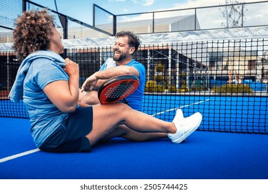 Mixed adult couple resting after playing padel on outdoor court. - Powered by Shutterstock