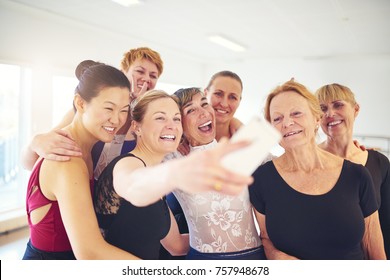 Mixed age group of women laughing while standing together taking selfies during ballet class in a dance studio - Powered by Shutterstock