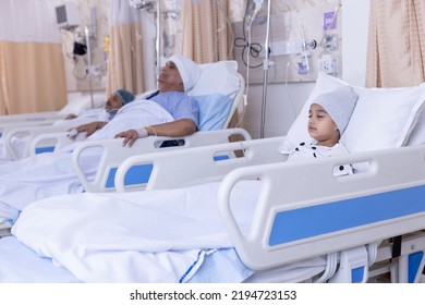 Mixed Age Range Patients Resting On Beds By Medical Equipment In Hospital Ward
