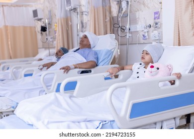 Mixed Age Range Patients Resting On Beds By Medical Equipment In Hospital Ward
