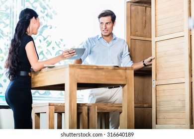 Mixed Asian Caucasian couple in furniture store or showroom calculating price, she is showing calculator to him