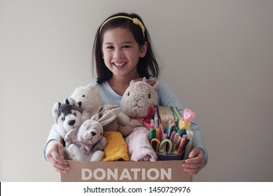 Mixed Asian young volunteer girl holding a box full of used toys, cloths, books and stationery for donation, Happy Charity,Asian community
