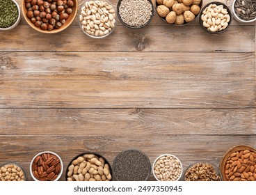 Mixed assorted nuts and seeds in various bowls on wooden table and space for text in the middle.
