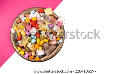 Mixed candies, top view colorful mixed candies. Almond sugar, wrapped luxury chocolate, cologne designed on vintage tray. Isolated half pink and white background with copy space. Sugar feast concept.
