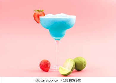 Mixed cocktails, party punch smoothies and frozen summer drinks concept with blue curacao mojito or daiquiri in margarita glass, strawberries and limes isolated on pink background