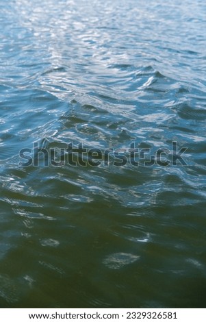 Mixed dark blue and dark turquoise surface of a lake, sea, ocean with ripples and sun glare. Water surface background, water texture closeup, vertical photo