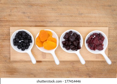 Mixed Dried Fruit And Berries In Ceramic Ramekins Including Apricots, Cherries, Blueberries And Cranberries Rich In Antioxidants And Vitamins, Overhead View On A Bamboo Cutting Board