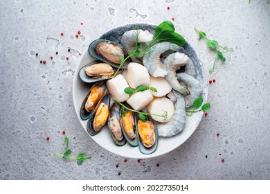 Mixed frozen seafood in plate on a gray stone background. Raw Shrimp, mussels and scallops