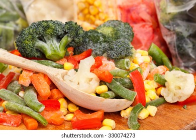 Mixed frozen vegetables on cutting board and plastic bags close up