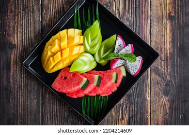 Mixed Fruits On A Black Plate With Mango, Watermelon, Green Apple And Dragon Fruit On A Wooden Background.