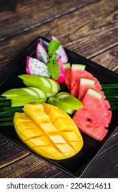 Mixed Fruits On A Black Plate With Mango, Watermelon, Green Apple And Dragon Fruit On A Wooden Background.