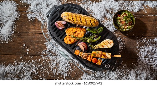 Mixed Grilled Fresh Vegetables Served On A Platter With Tofu Kebabs, Corn On The Cob, Sweet Potato And Salad Outdoors On A Winter Table With Snow In A Top Down View