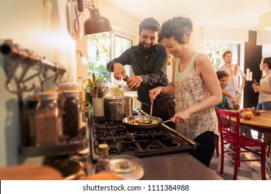 Mixed group of friends having fun while cooking a meal in a warm and welcoming kitchen. a couple takes care of the pots on the stove , while the sun comes in through the window - Powered by Shutterstock