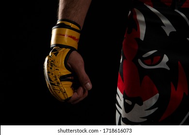 Mixed martial arts (MMA) fighter. Detail of the yellow glove with tiger pants on black background. Mixed martial arts concept.