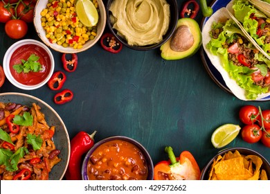 Mixed mexican food background. Party food. Guacamole, nachos, fajita, meat tacos, salsa, peppers, tomatoes on a wooden table. Space for text. Top view. Tex-mex cuisine. Assorted appetizers. Food frame